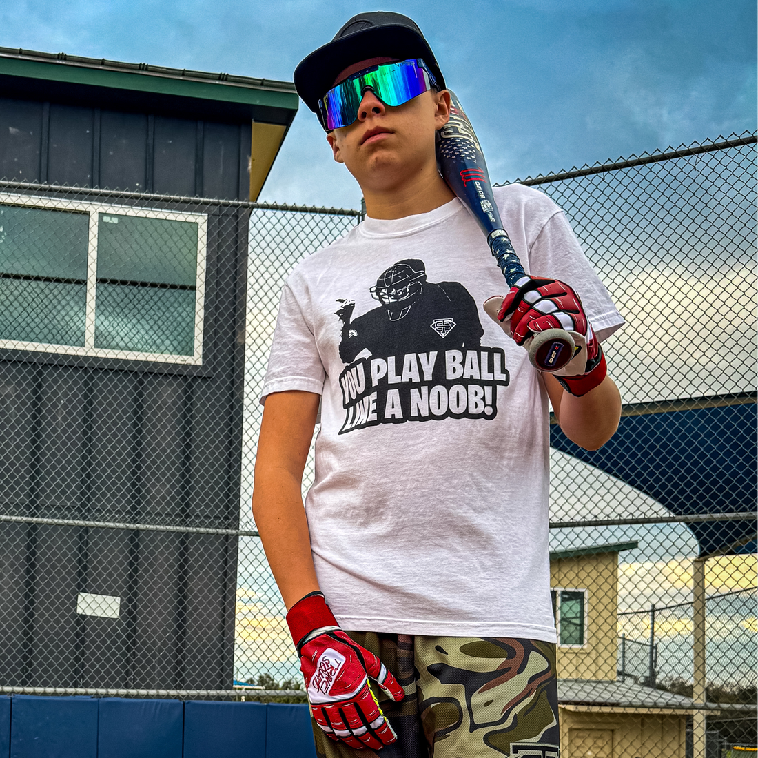 A white crew neck t-shirt with a graphic print of a baseball player and the text 'YOU PLAY BALL LIKE A NOOB!'